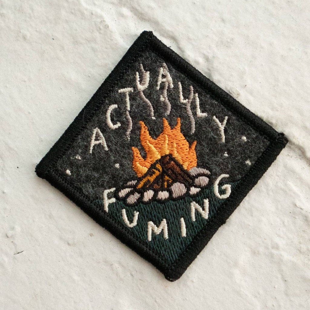 Embroidered patch with a campfire design and text on a textured white background