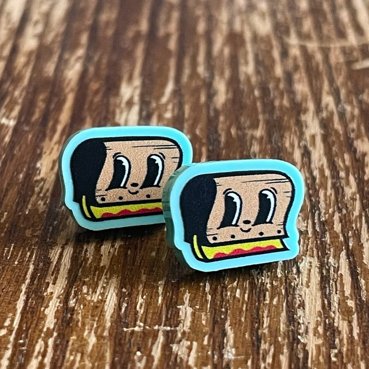 Two cartoon-style silkscreen squeegee cartoon earrings on a wooden surface with 'Rapscallion' branding.