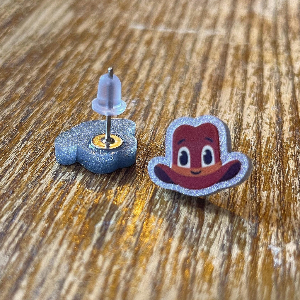 Cartoon character cowboy hat earrings on a wooden surface with 'RAPSCALLION' branding.