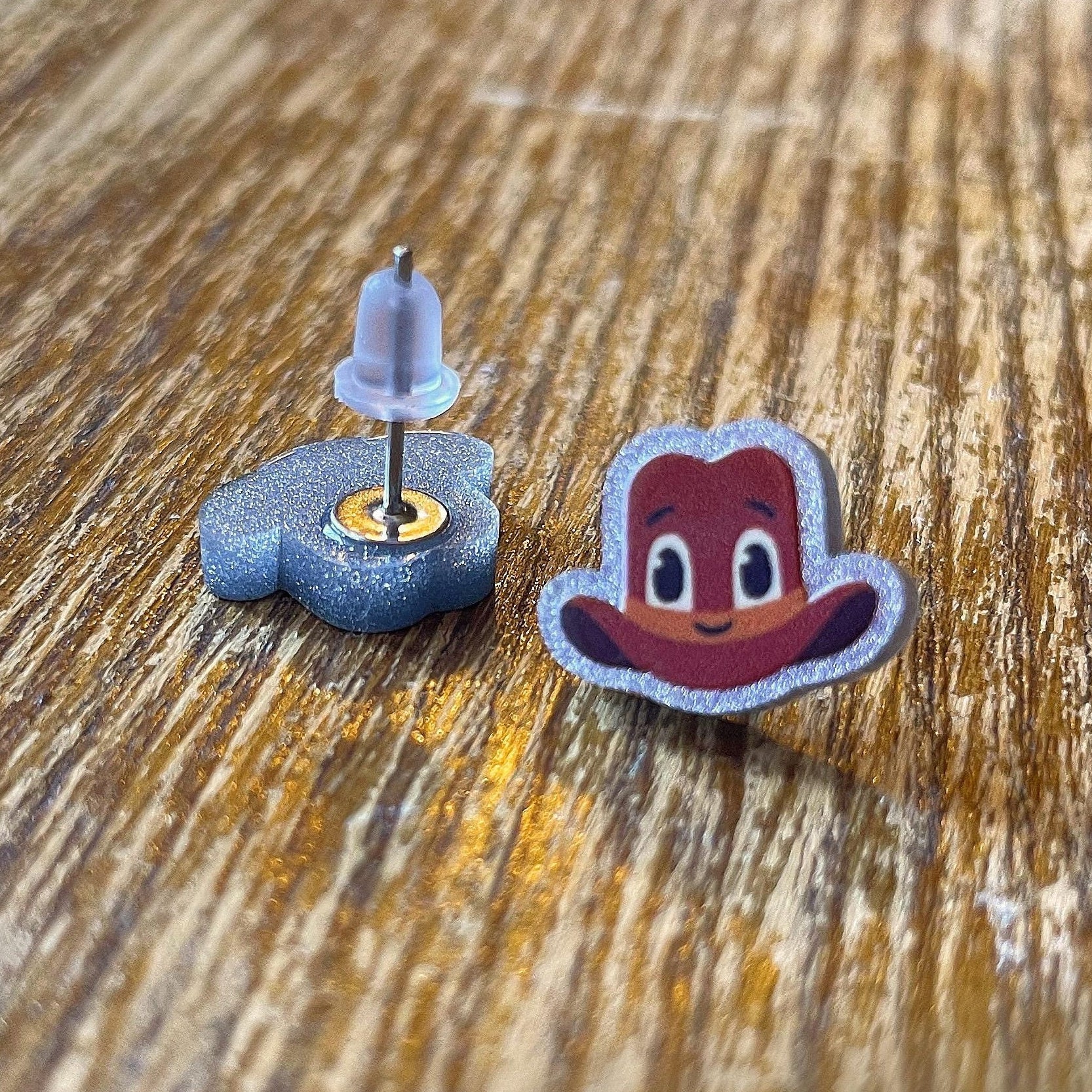 Cartoon character cowboy hat earrings on a wooden surface with 'RAPSCALLION' branding.