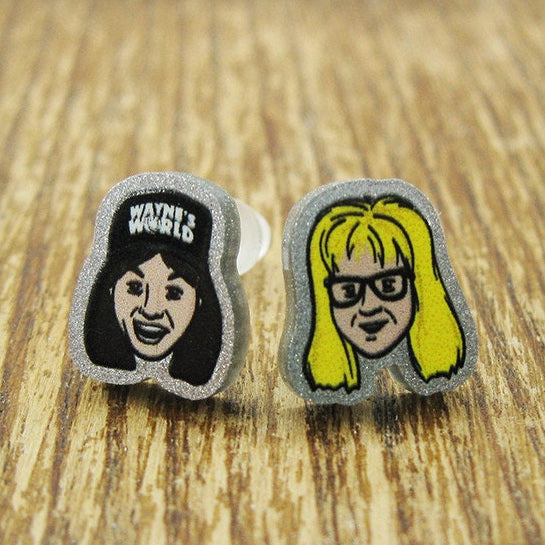Two earrings with cartoon-style faces Wayne garth on a wooden surface, featuring the brand 'Rapscallion'.