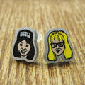 Two earrings with cartoon-style faces Wayne garth on a wooden surface, featuring the brand 'Rapscallion'.